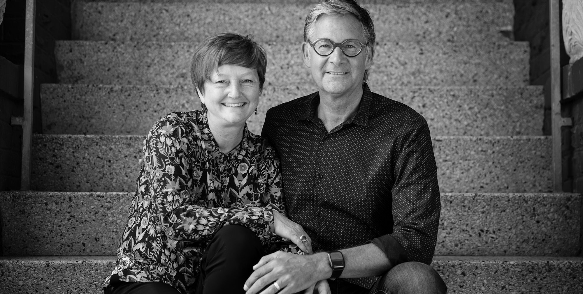 A portrait of Tina and her partner Paul sitting on steps together in black and white