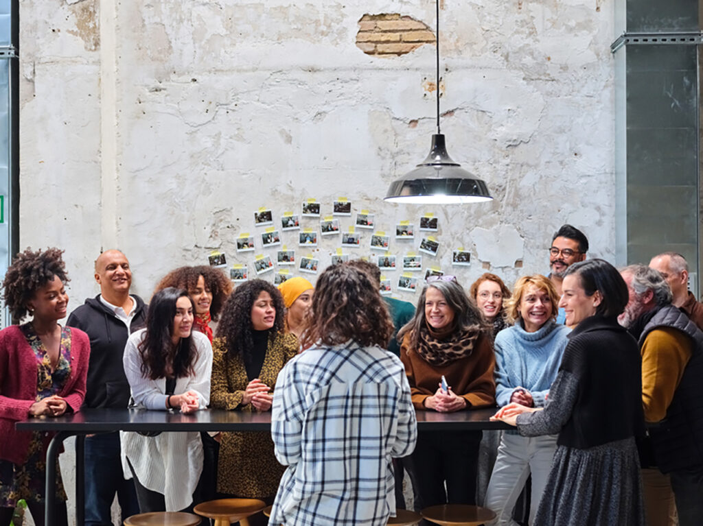 Group of colleagues standing at long black desk, having a casual meeting.