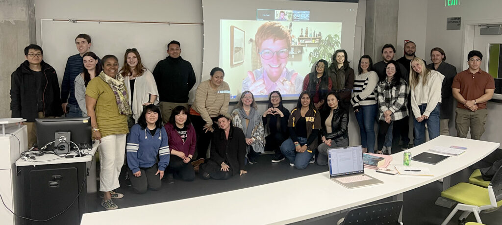 a photo of a group in a conference room with Tina joining by Zoom