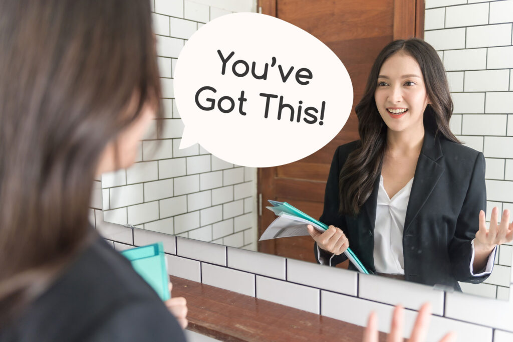 a woman looking at herself in the mirror, saying "You've got this!"